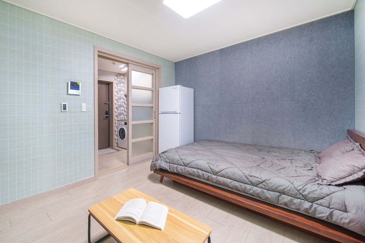 Een compacte, moderne slaapkamer met een bed, een bureau en een wasmachine in de hoek.