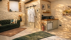 Une pièce chaleureuse avec un mur en pierre, un canapé vert, un banc en bois, une petite kitchenette et une fenêtre.