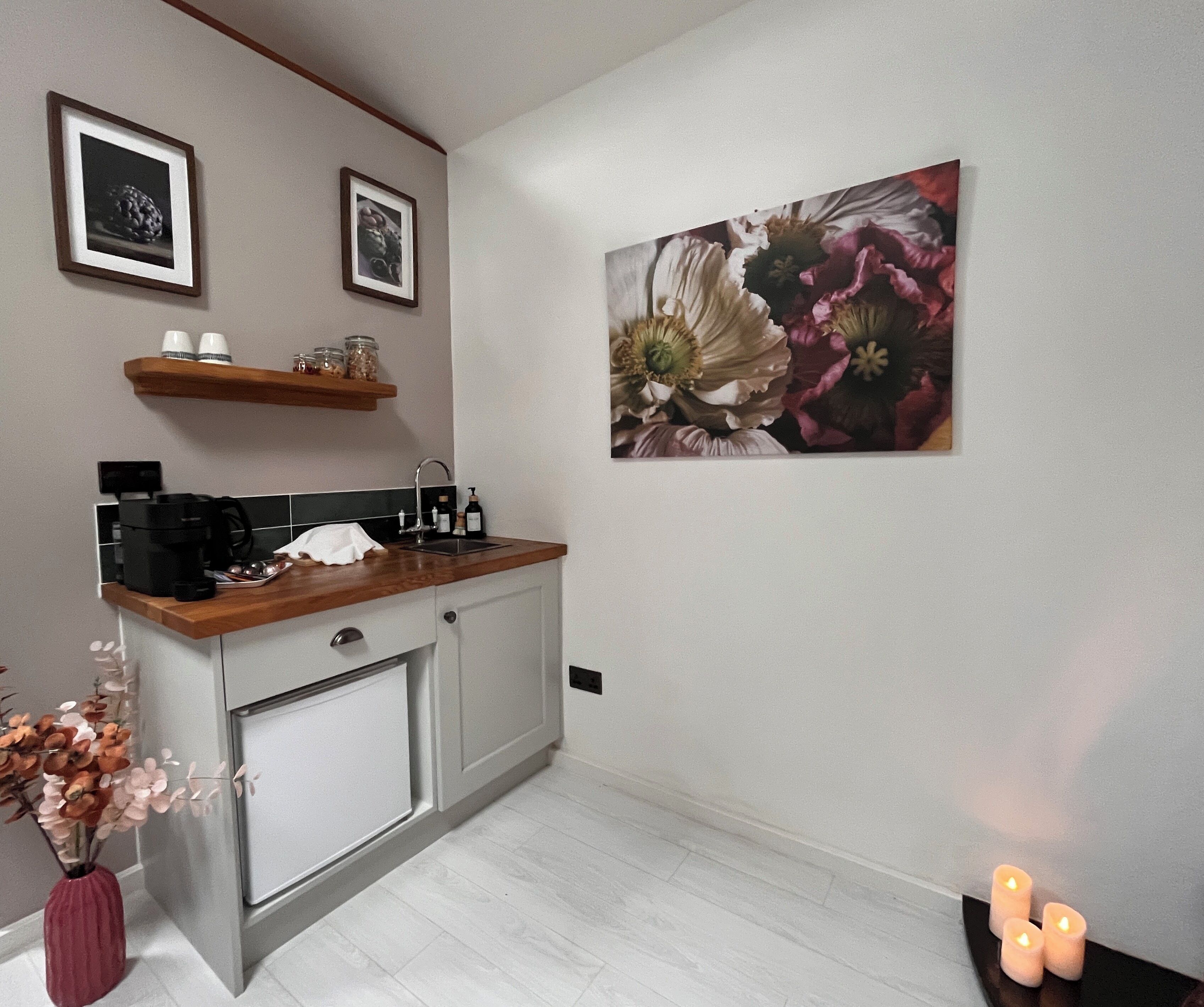 Une cuisine équipée d’une machine à café, d’un évier et d’un plan de travail en bois. Deux tableaux encadrés sont accrochés au mur, au-dessus du plan de travail.