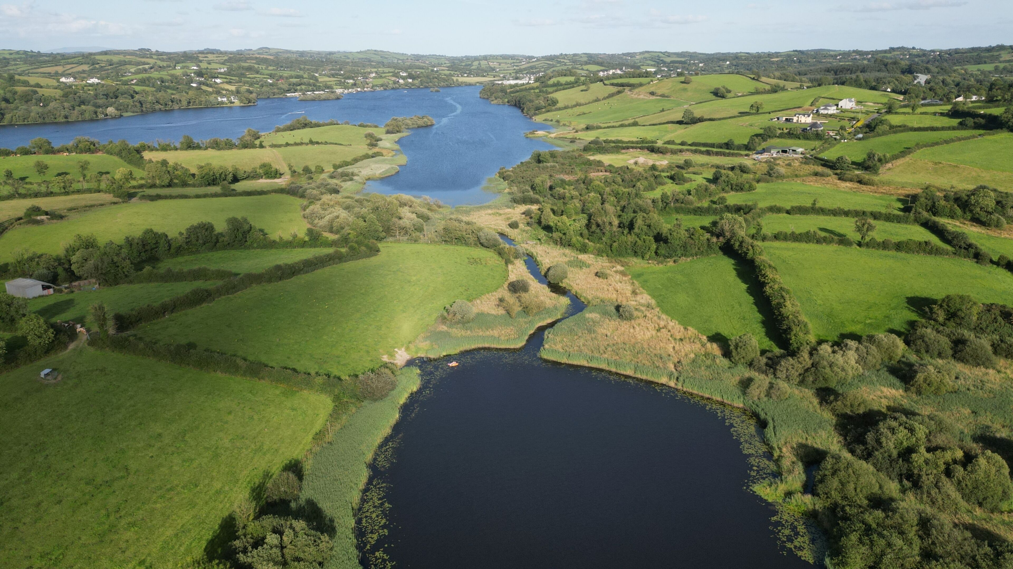 Luchtbeeld van een landelijk gebied met een rivier, groene velden en verspreide gebouwen.