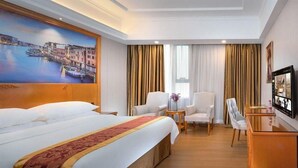 Ein Hotelzimmer mit einem großen Bett, zwei Sesseln, einem kleinen Tisch und einem Fernseher.