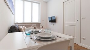 Un comedor con una mesa dispuesta para dos personas, un televisor montado en la pared y una ventana con persianas.