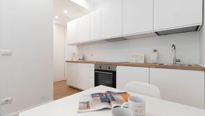 Una cocina moderna con armarios blancos, encimera de madera, pileta de acero inoxidable y horno. Hay una revista sobre la mesa y dos tazas.