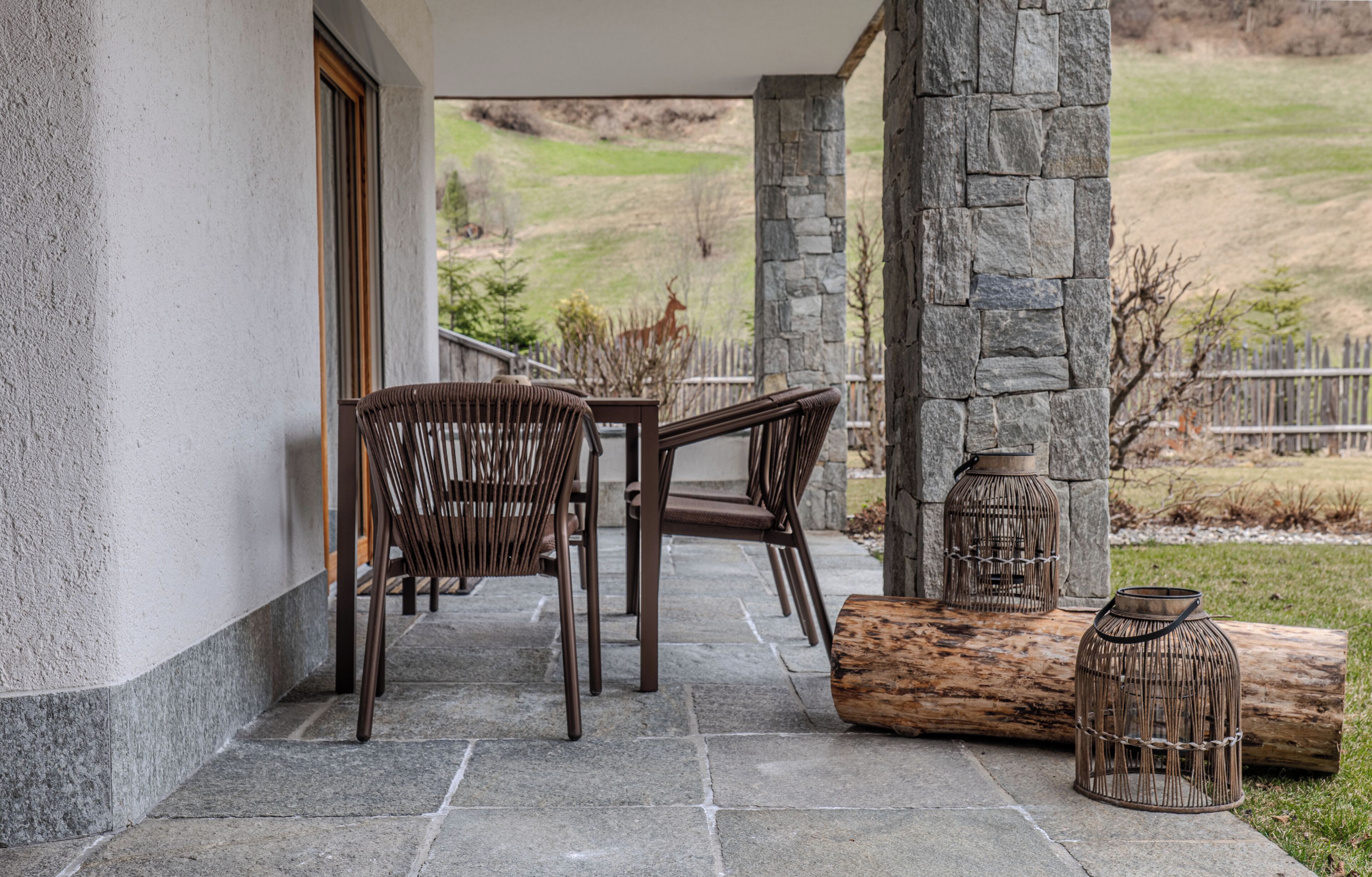 Un patio cubierto con suelo de piedra, sillas de mimbre, una mesa de madera y faroles decorativos.