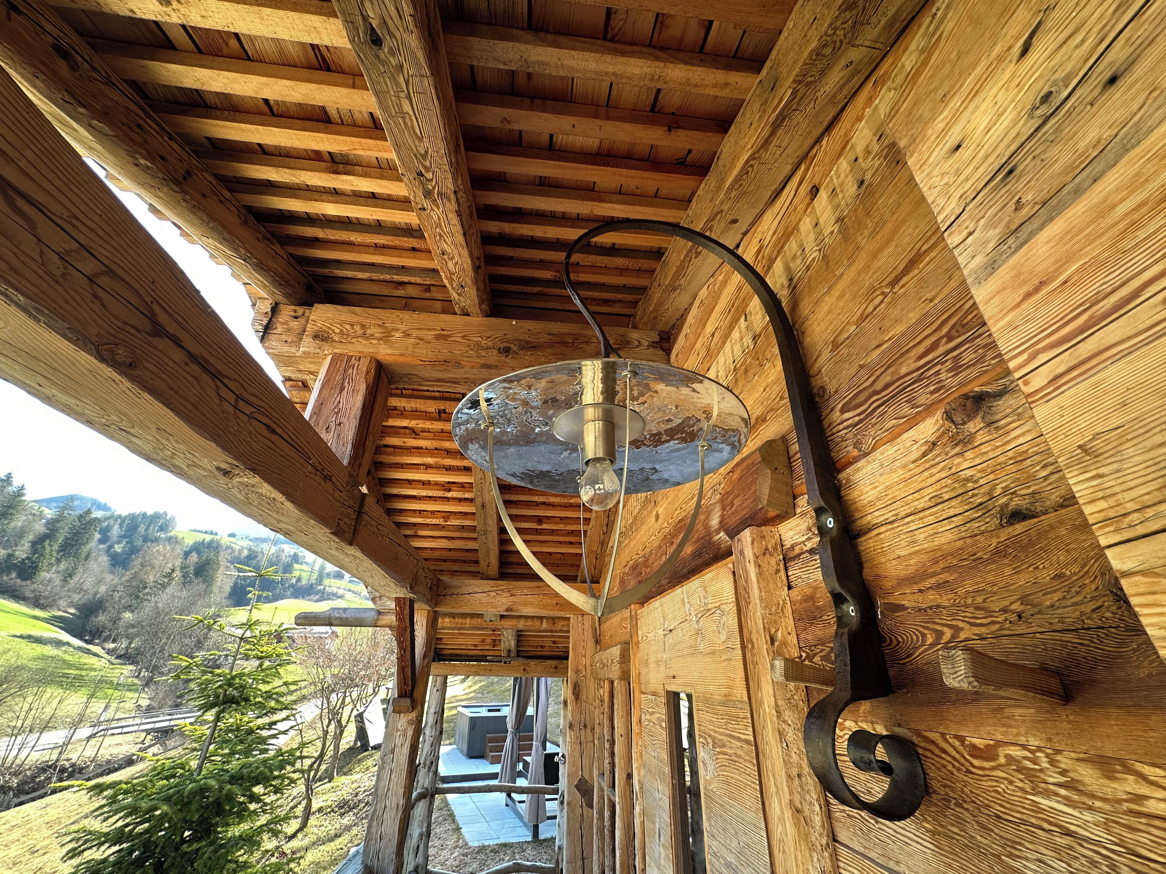 A wooden interior with a ceiling fan, a view of a wooden structure outside, and a metal light fixture.
