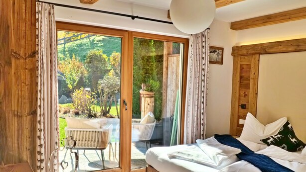 A bedroom with a large sliding glass door leading to a patio with outdoor furniture and a garden view. - Alpine Mountain Chalet (Marebbe)