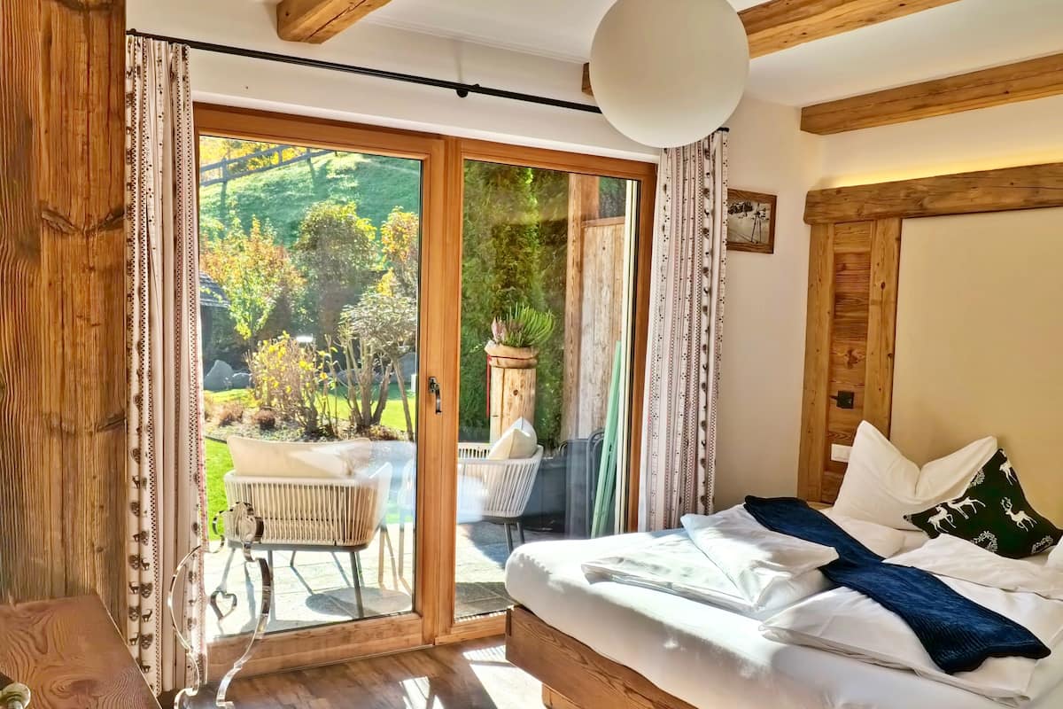 A bedroom with a large sliding glass door leading to a patio with outdoor furniture and a garden view.