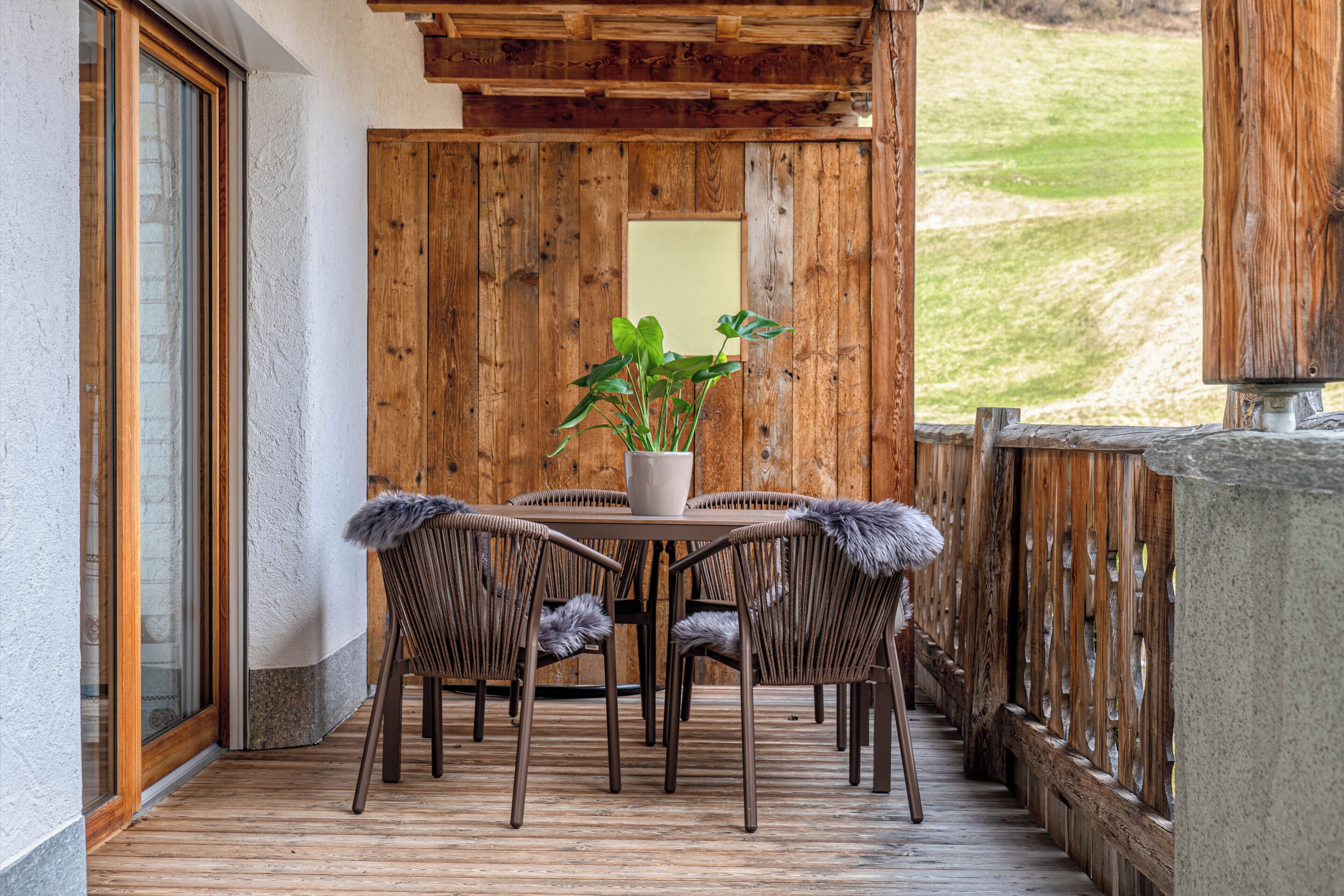 Une terrasse en bois avec une table et des chaises, un pot de fleurs et une vue sur une zone herbeuse.