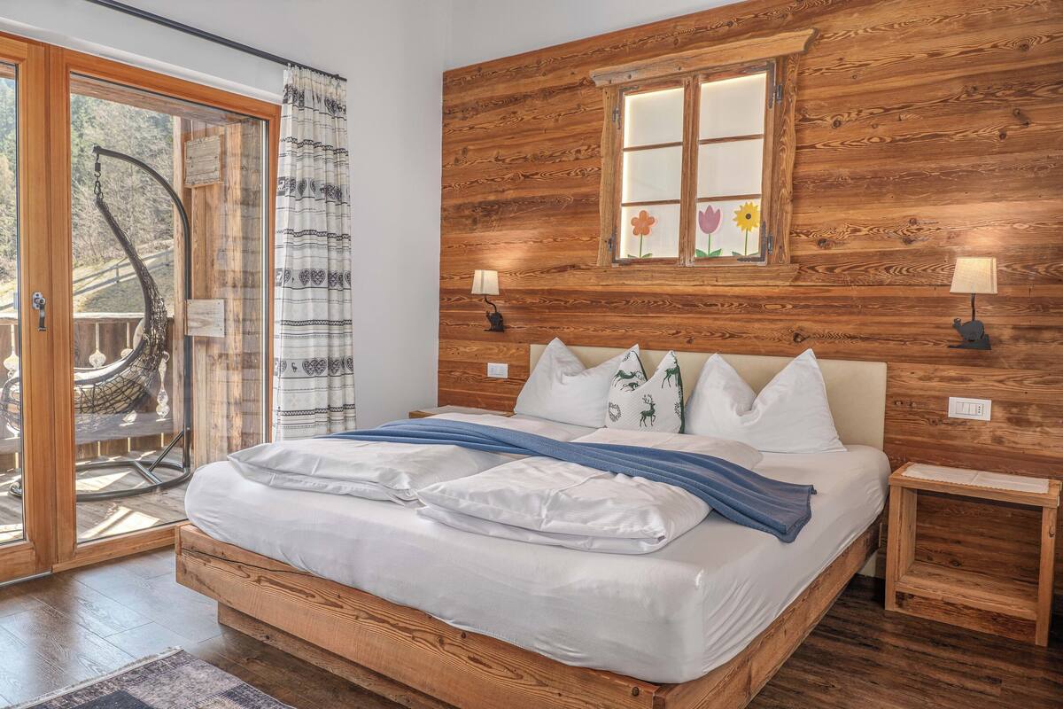 A wooden-framed bed with white bedding, two bedside lamps, and a window with a flower decoration.