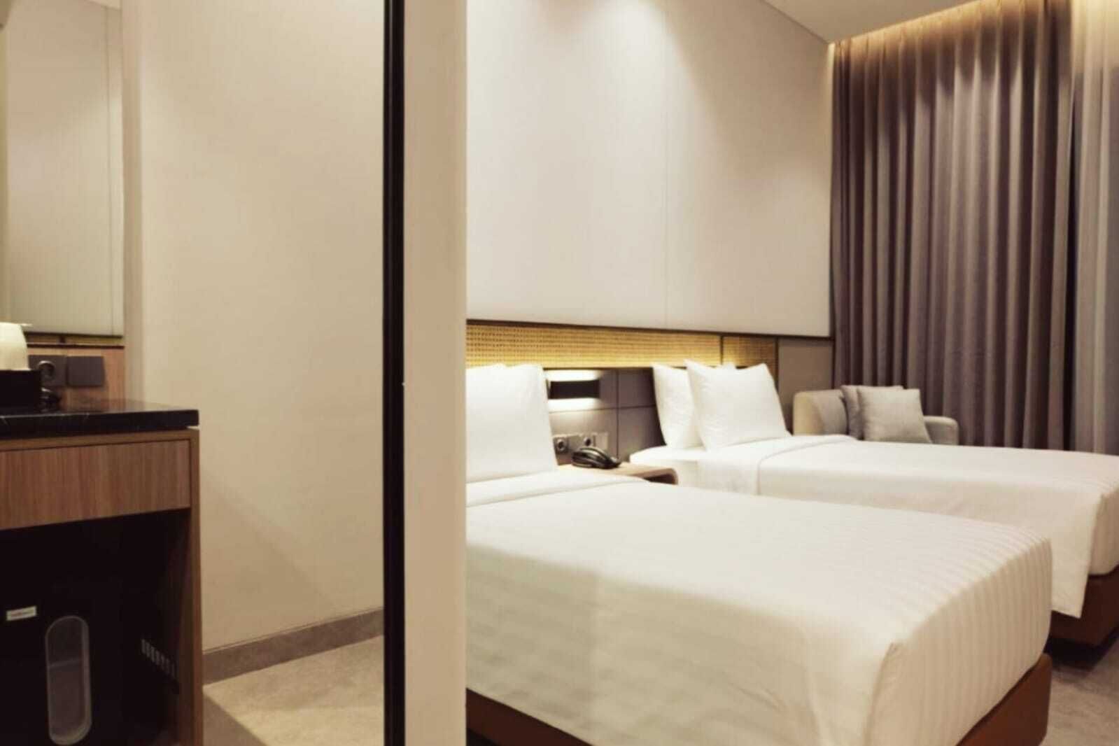 A hotel room with two beds, a wooden desk, and a large mirror.