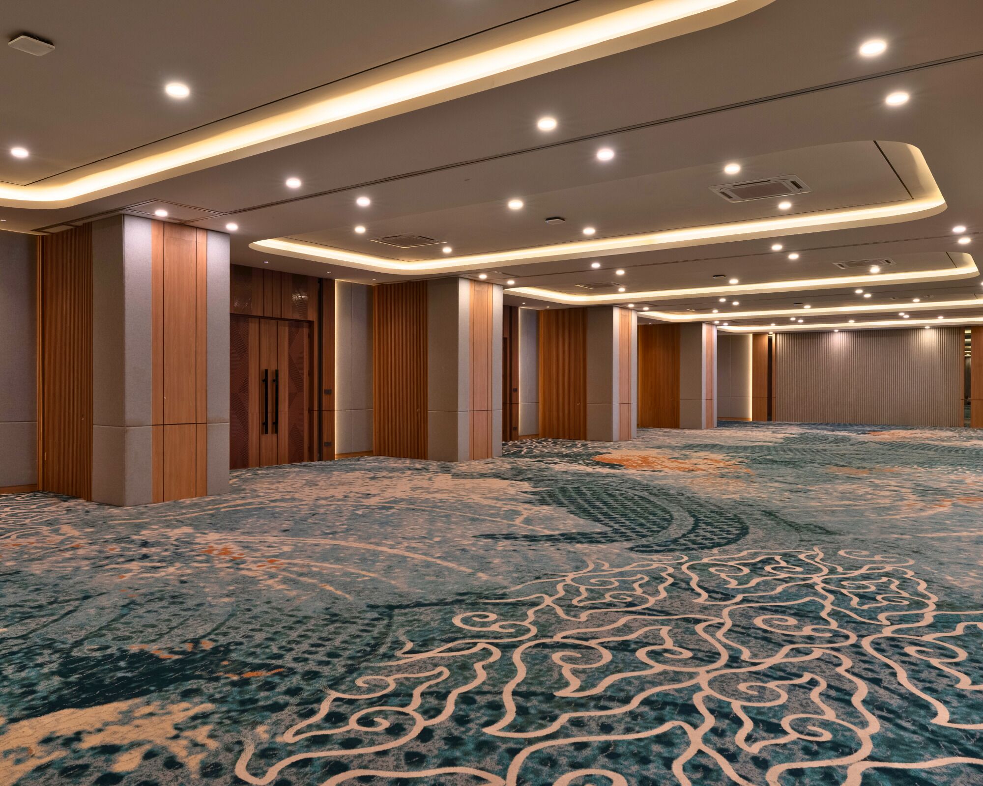 A spacious hotel lobby with a patterned carpet, wooden paneling, and recessed lighting.