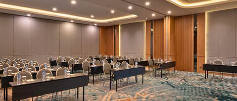 Un salón de conferencias con varias mesas y sillas, equipado con botellas de agua y vasos, y una alfombra estampada.
