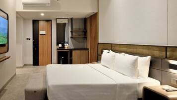 Ein modernes Hotelzimmer mit einem großen Bett, einem Nachttisch, einem kleinen Schreibtisch, einem Spiegel und einem an der Wand befestigten Fernseher.