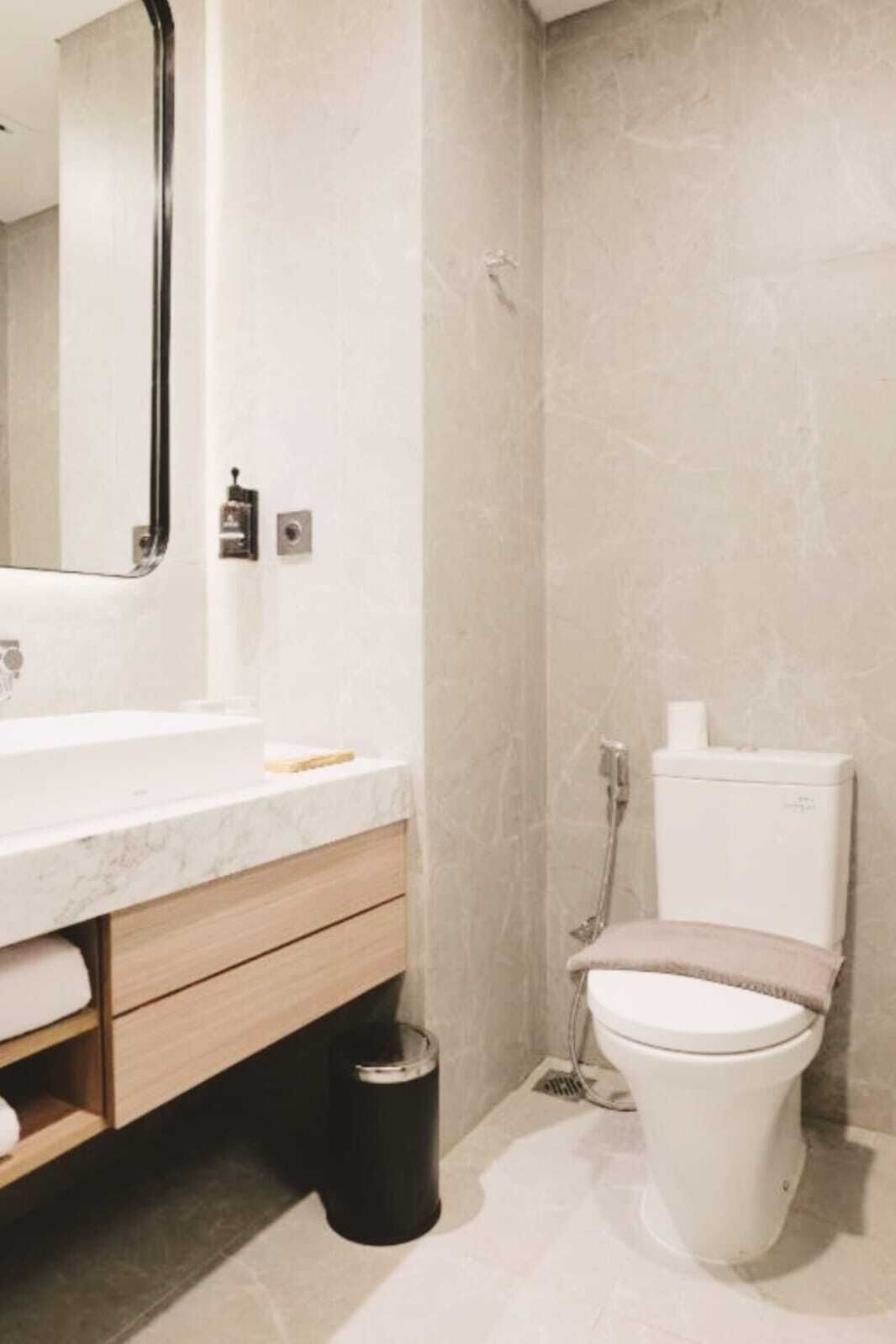 Une salle de bain moderne avec un comptoir en marbre, un meuble en bois et des toilettes dotées d’un abattant beige.