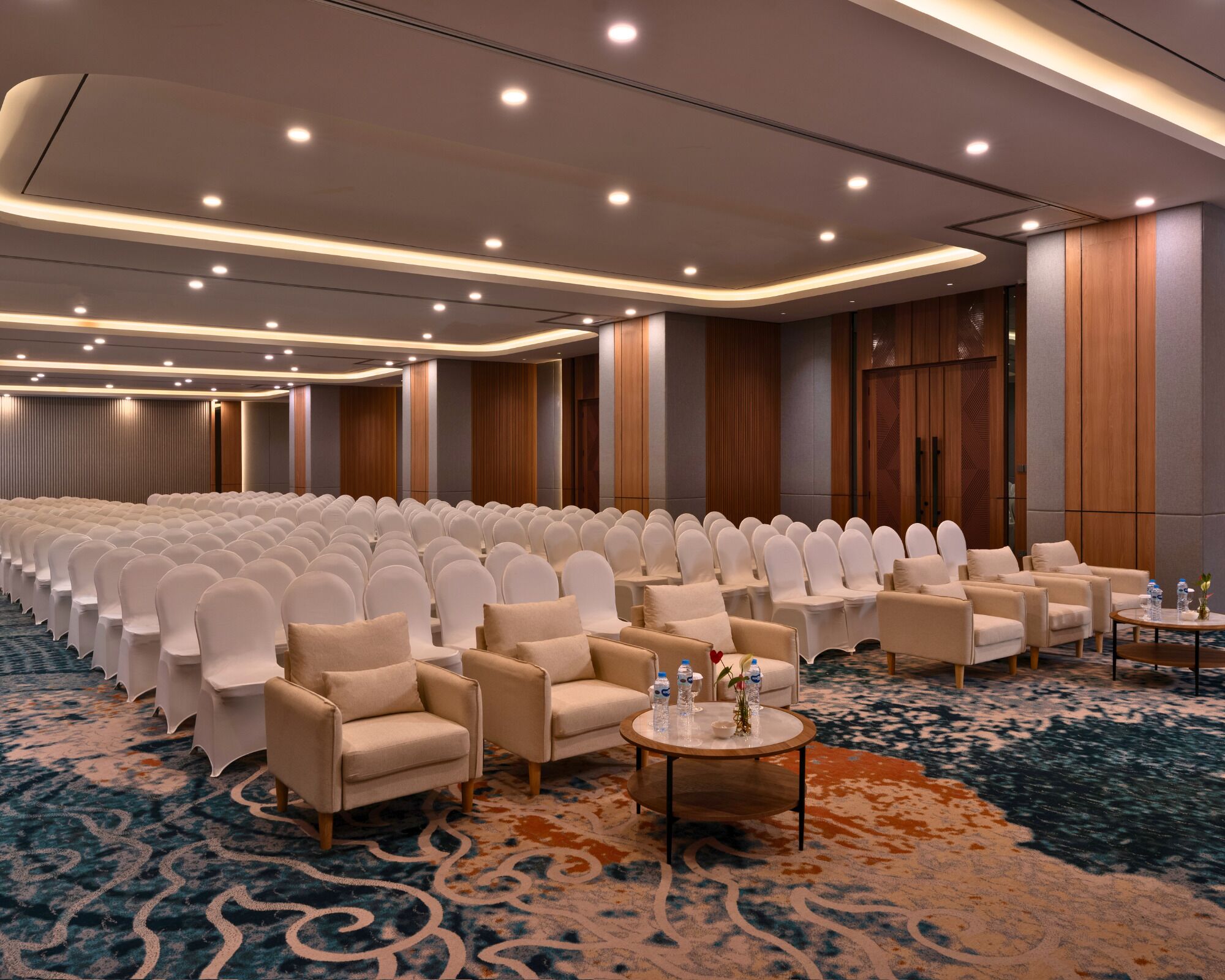 A conference room with rows of white chairs, a carpeted floor, and a wooden panel wall.