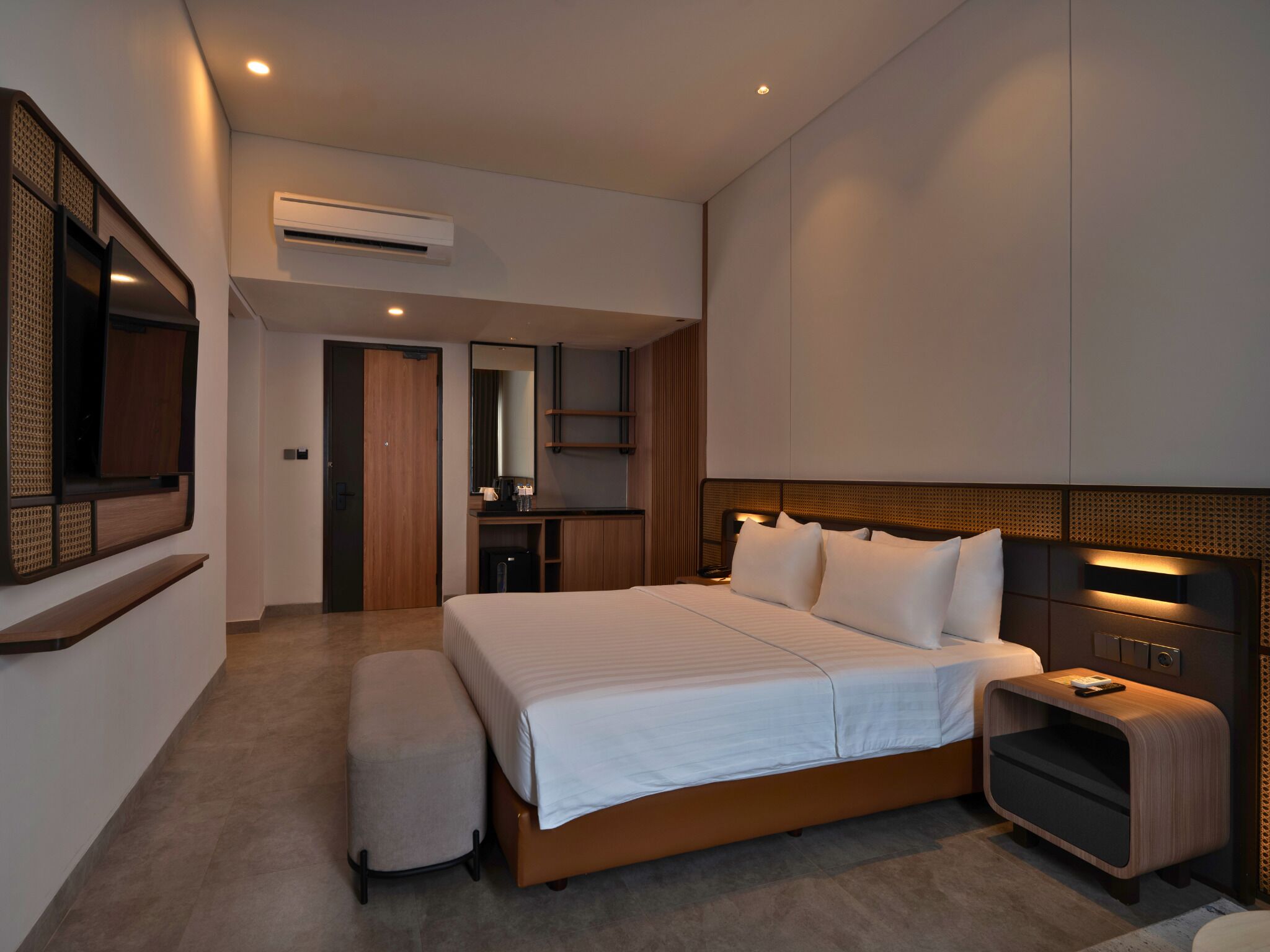 A modern hotel room with a large bed, a bedside table, a small desk, and a wall-mounted TV.