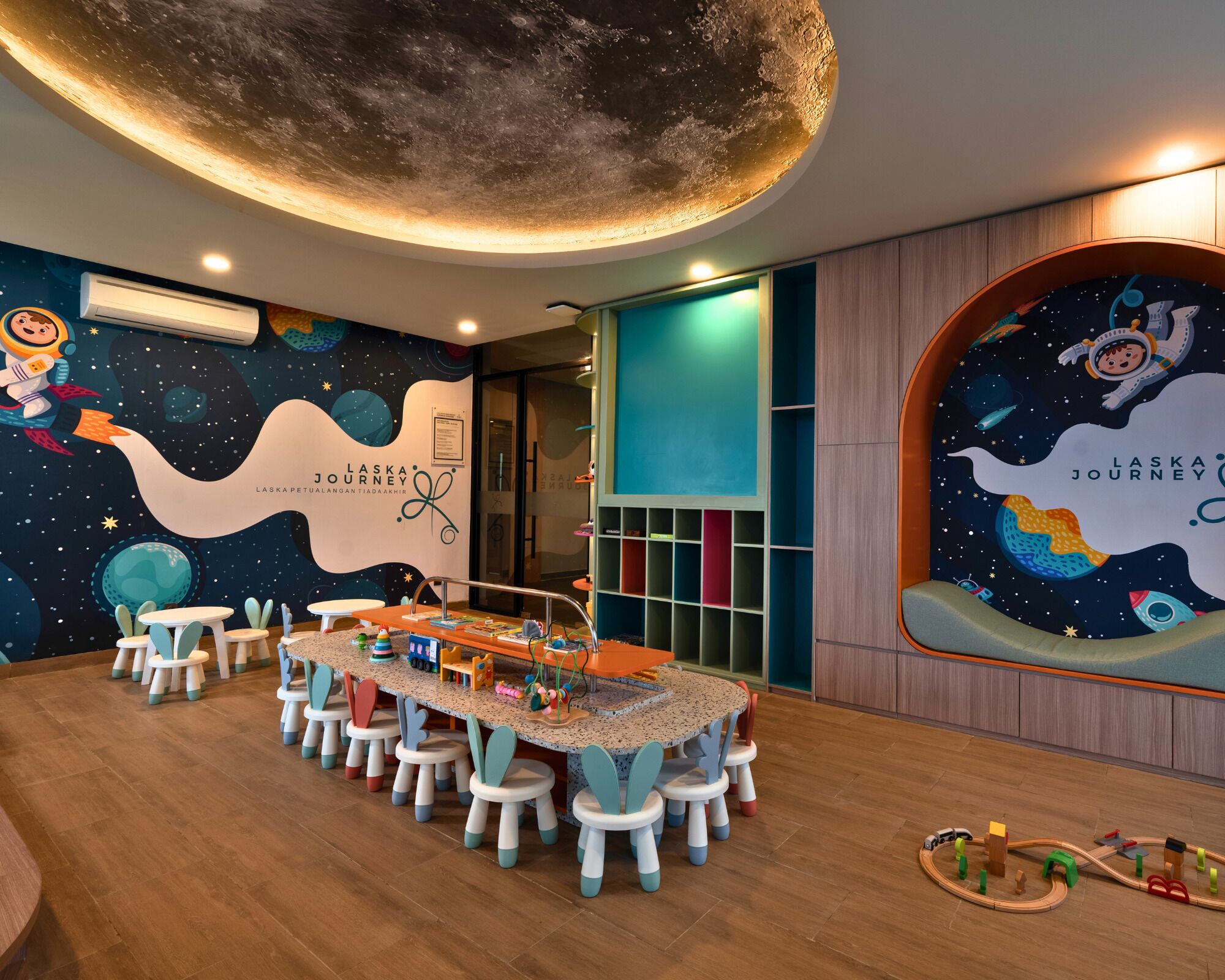 Un cuarto de juegos infantil con un mural alusivo al espacio, una mesa redonda con taburetes y una zona de juegos llena de juguetes.