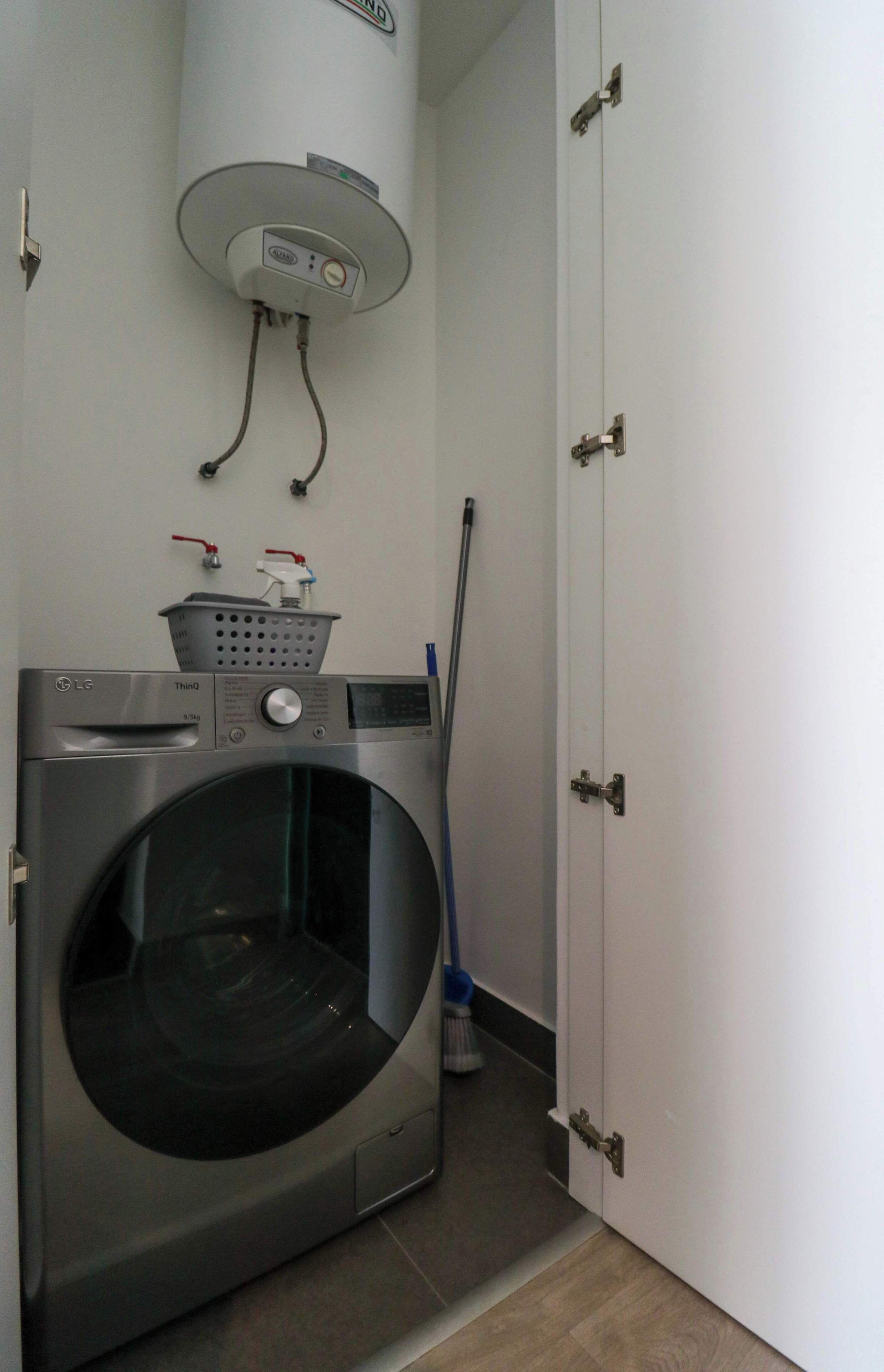 A compact laundry area with a front-loading washing machine, a wall-mounted dryer, and a broom leaning against the wall.