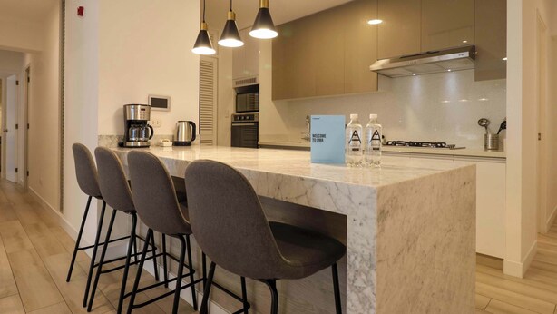 A modern kitchen with a marble island, bar stools, and pendant lighting.