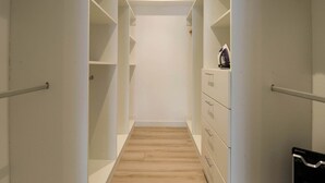 A narrow walk-through closet with wooden flooring, white walls, and a metal handrail.