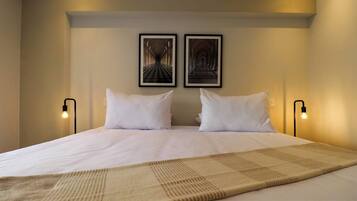 A neatly made bed with white linens and a beige throw blanket, two framed pictures on the wall, and bedside lamps.