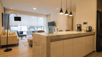A modern kitchen with a marble countertop, a black refrigerator, and a coffee maker.