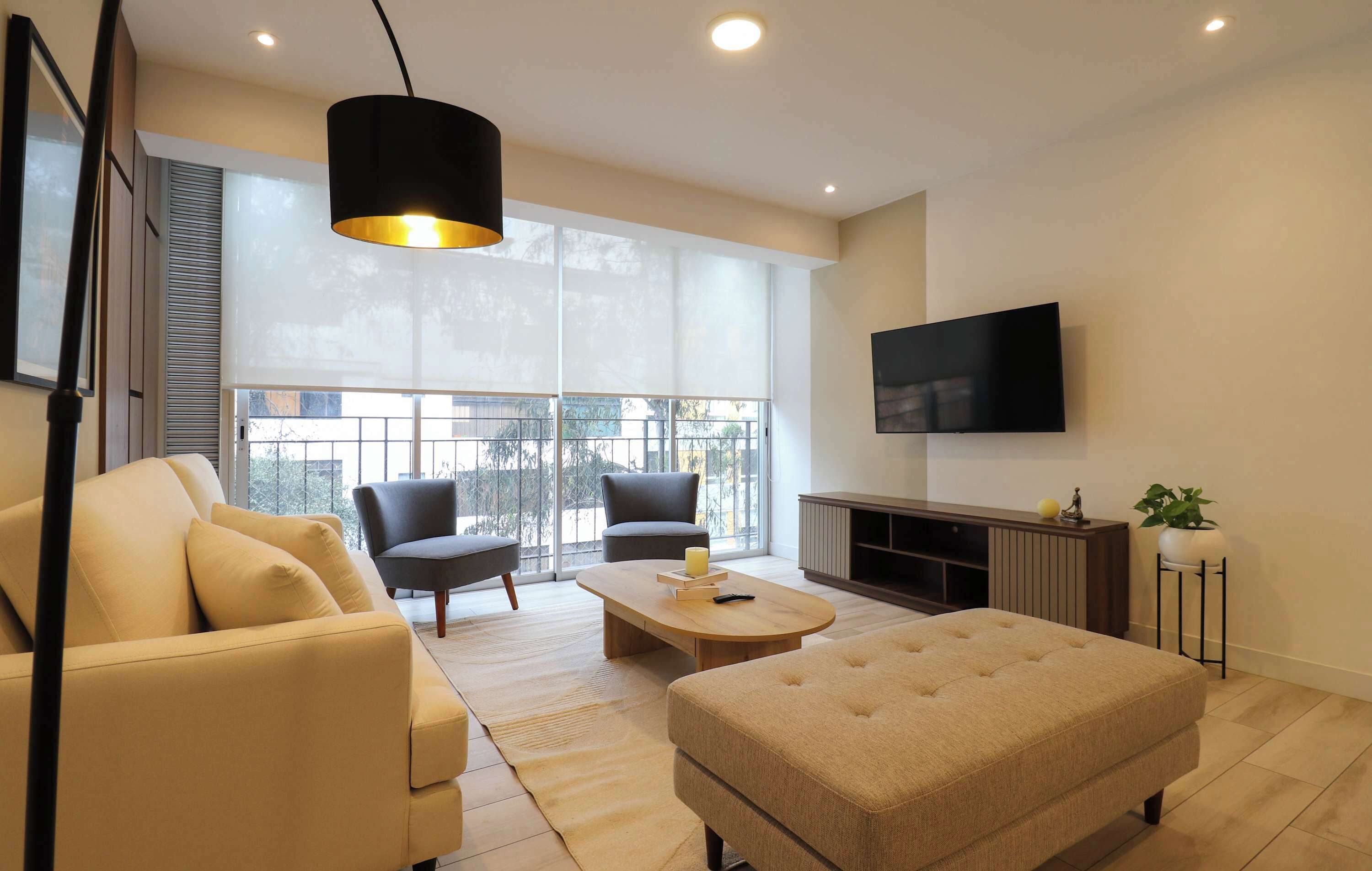 A modern living room with a sofa, armchairs, a coffee table, and a TV mounted on the wall.