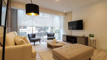 A modern living room with a sofa, armchairs, a coffee table, and a TV mounted on the wall.