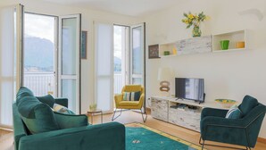 A modern living room with a sofa, armchairs, a TV, and a balcony with a view of mountains. - Lakefront Contemporary (Griante)