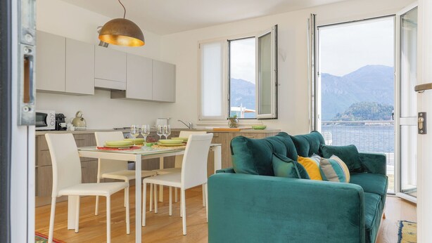 A modern living room with a teal sofa, white chairs, and a dining table set for four. - Lakefront Contemporary (Griante)