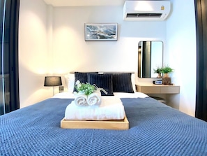 A hotel room with a bed, a bedside table, a lamp, a mirror, an air conditioner, and a framed picture on the wall. - Sea View Edge Central Pattaya (Pattaya)