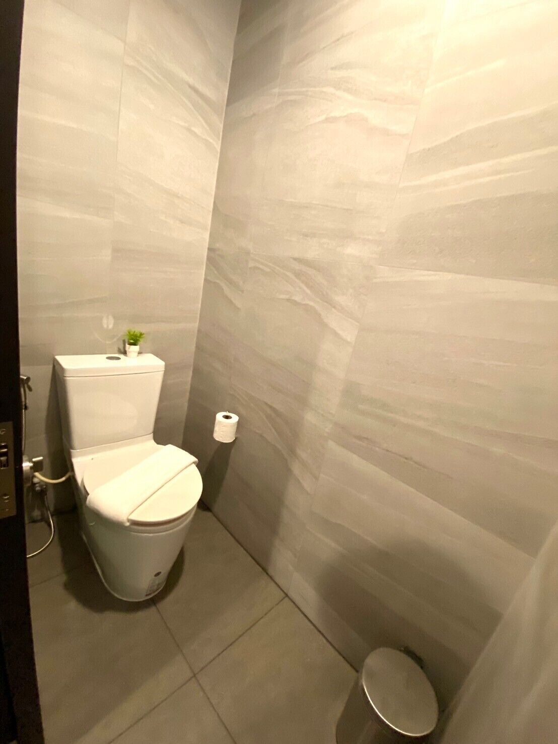 A small, modern bathroom with a toilet, a small trash bin, and a wall-mounted toilet paper holder.