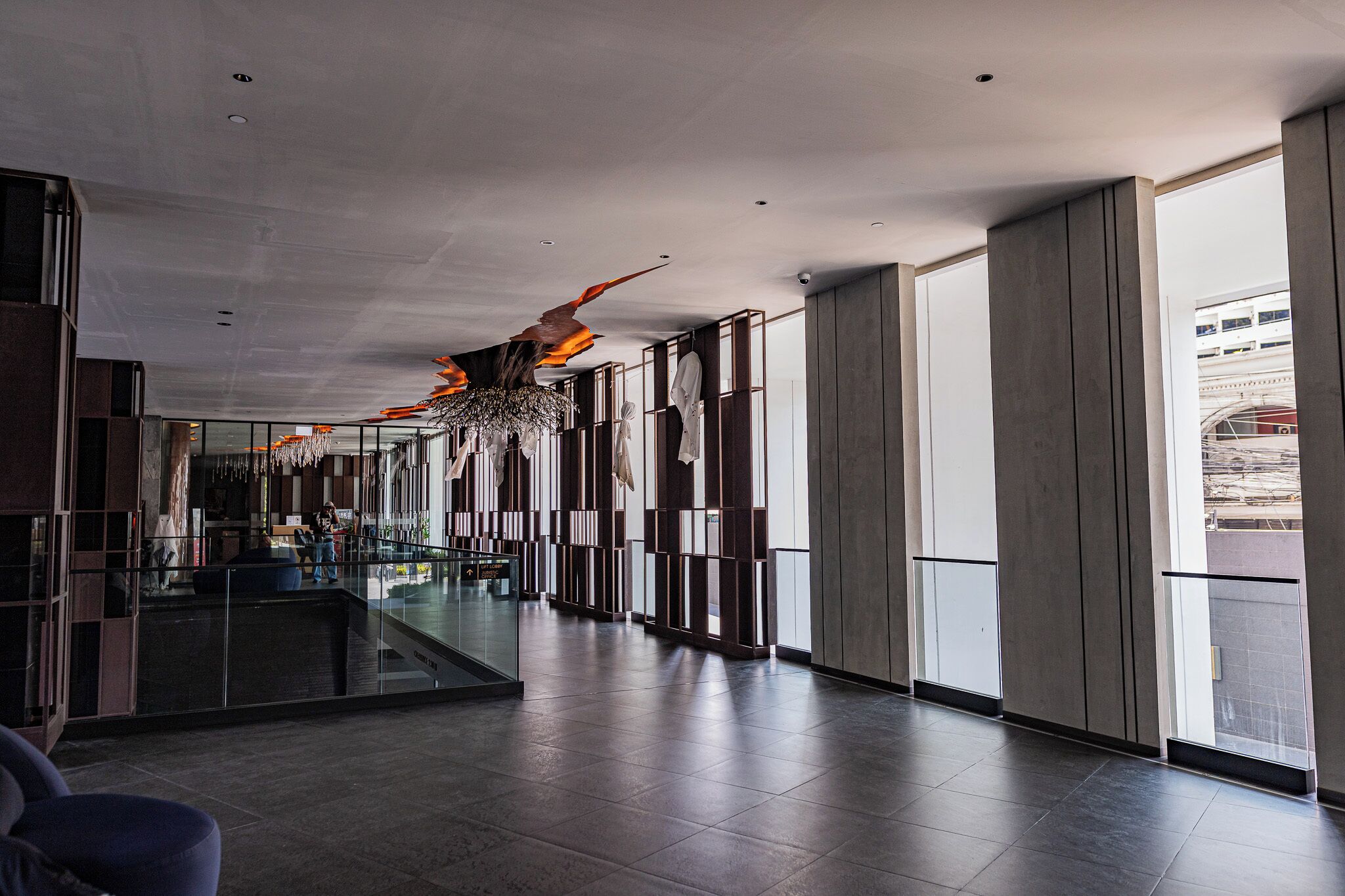 A spacious lobby with a modern design, featuring a long corridor, large windows, and a unique ceiling sculpture.