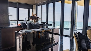 Un comedor moderno con una mesa de vidrio, sillas y vista al mar a través de amplios ventanales.