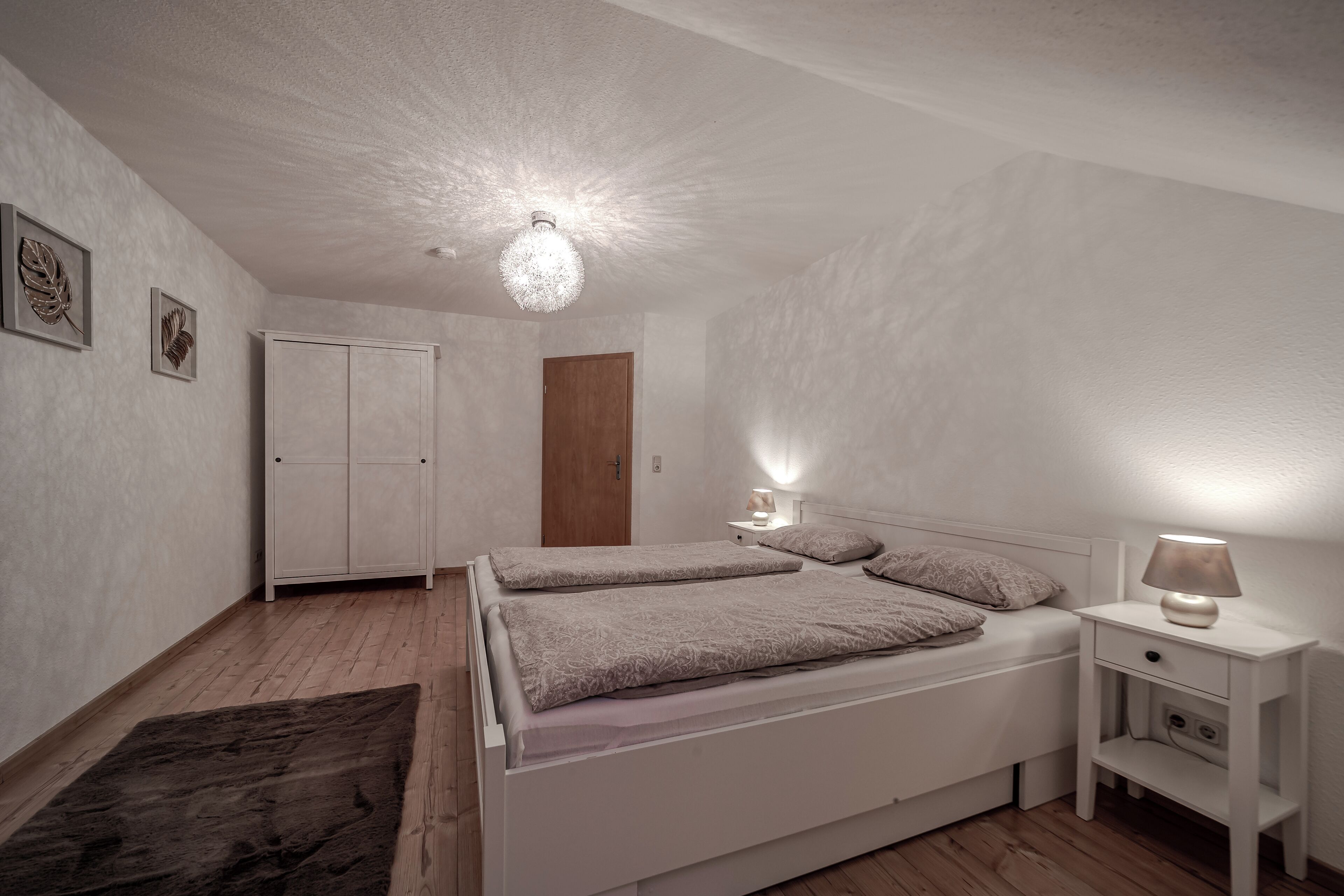 Un dormitorio con cama, mesitas de noche, armario y lámpara en el techo.