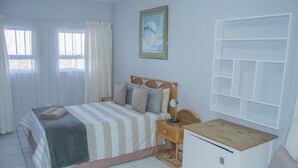 Ein Schlafzimmer mit Bett, Nachttisch, Lampe und einem kleinen weißen Schrank.