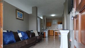 Ein Wohnzimmer mit braunem Ledersofa, einem weißen Podest und einer Küche im Hintergrund.