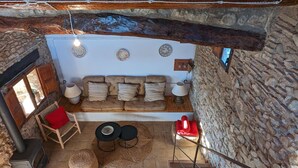 Un interior rústico con pared de piedra, vigas de madera, chimenea, sofá y una pequeña mesa.