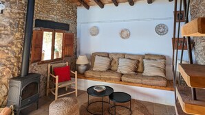 Una habitación rústica con pared de piedra, vigas de madera, chimenea de piedra, un sofá y una mesita con lámpara.