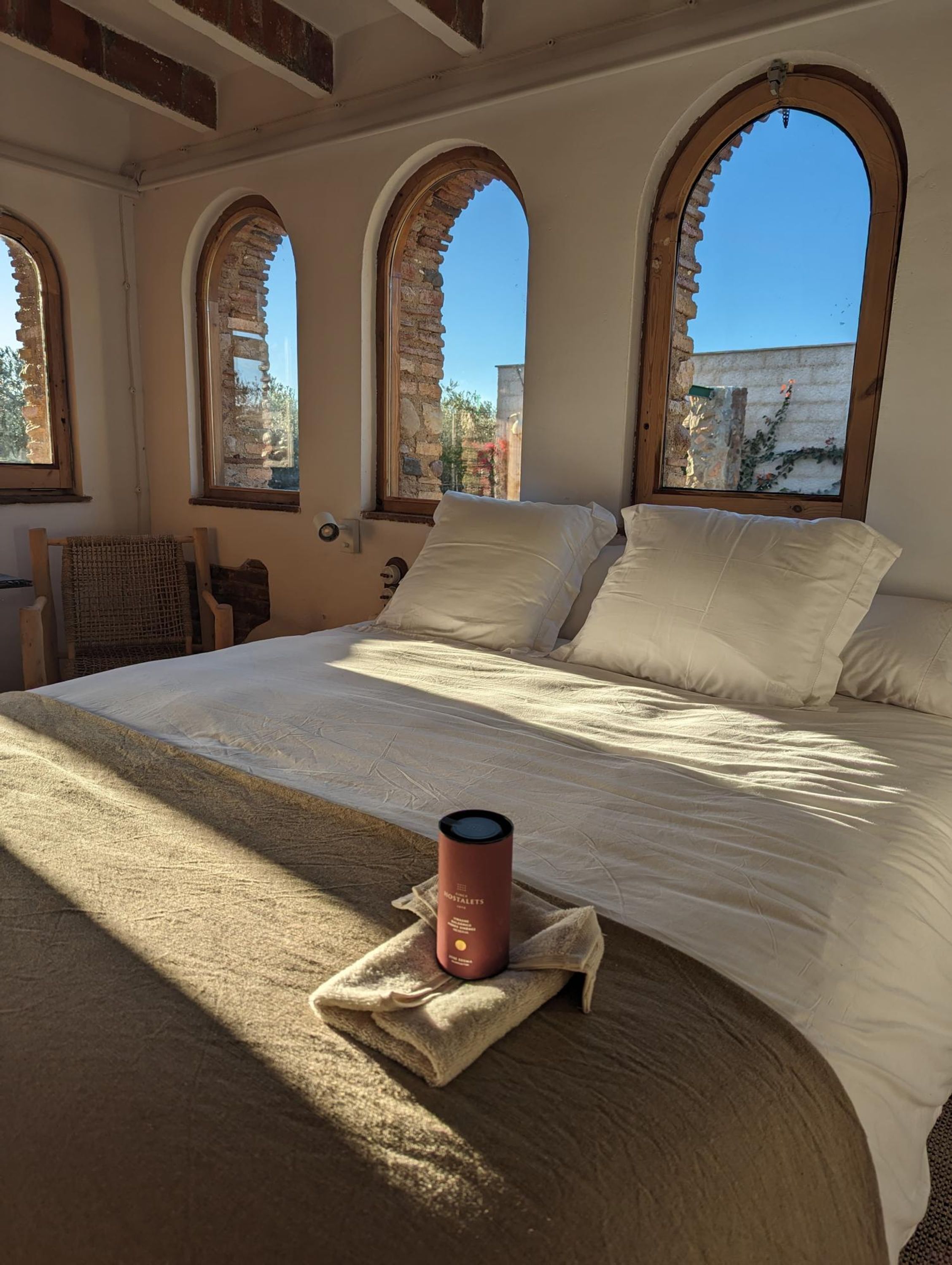 Un dormitorio con una cama grande, tres ventanas de arco, una silla y una mesita de noche.