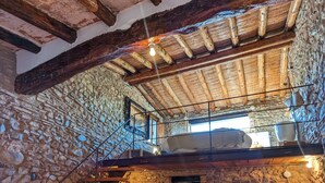 Una habitación rústica con paredes de piedra, una escalera de madera, un barril de madera y una mesa dispuesta para comer.