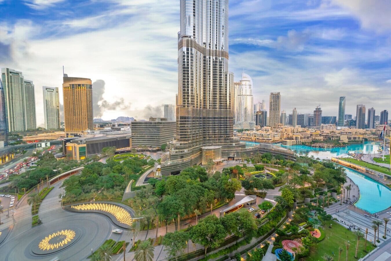 A modern cityscape with a prominent skyscraper, lush green parks, and a large water feature.