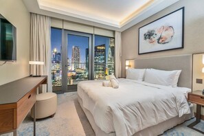 A hotel room with a large bed, a desk, a chair, a TV, and a city view through floor-to-ceiling windows. - Family 3BR Flat | Free Parking, Gym, Pool & Burj Views (Dubai)