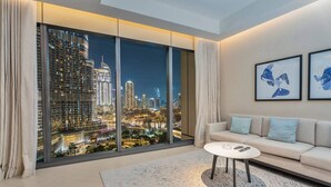 A modern living room with a large window offering a city view, a sofa, a coffee table, and two framed artworks. - Family 3BR Flat | Free Parking, Gym, Pool & Burj Views (Dubai)