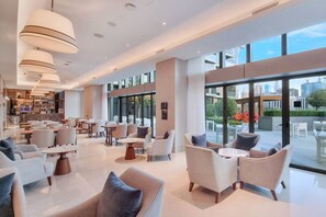 A spacious indoor area with multiple seating arrangements, large windows, and a visible outdoor patio area. - Family 3BR Flat | Free Parking, Gym, Pool & Burj Views (Dubai)