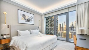 A modern hotel room with a large bed, a city view, a desk, and a chair. - Family 3BR Flat | Free Parking, Gym, Pool & Burj Views (Dubai)