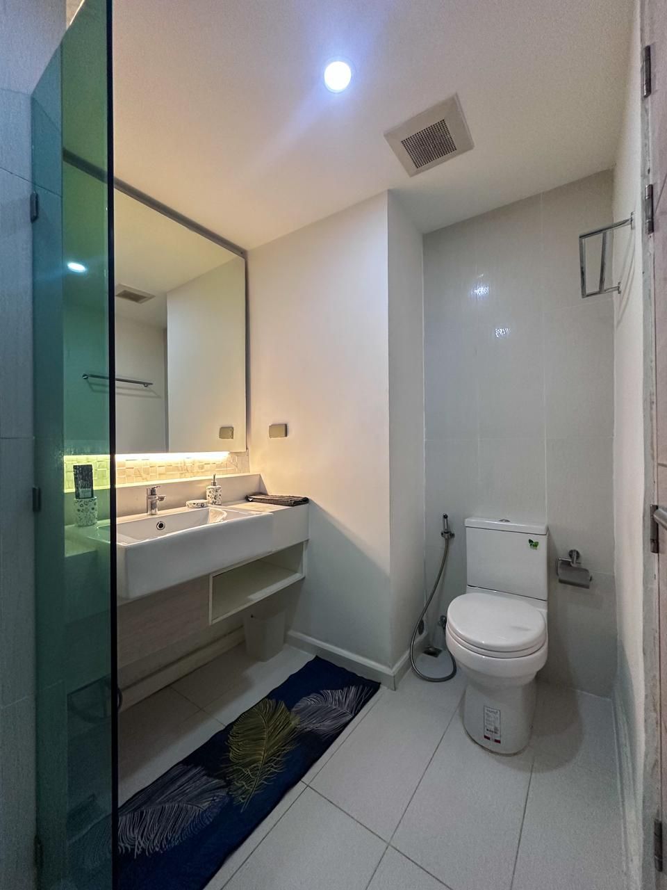 Un baño moderno con cabina de ducha de vidrio, un lavamanos blanco con espejo y un inodoro.