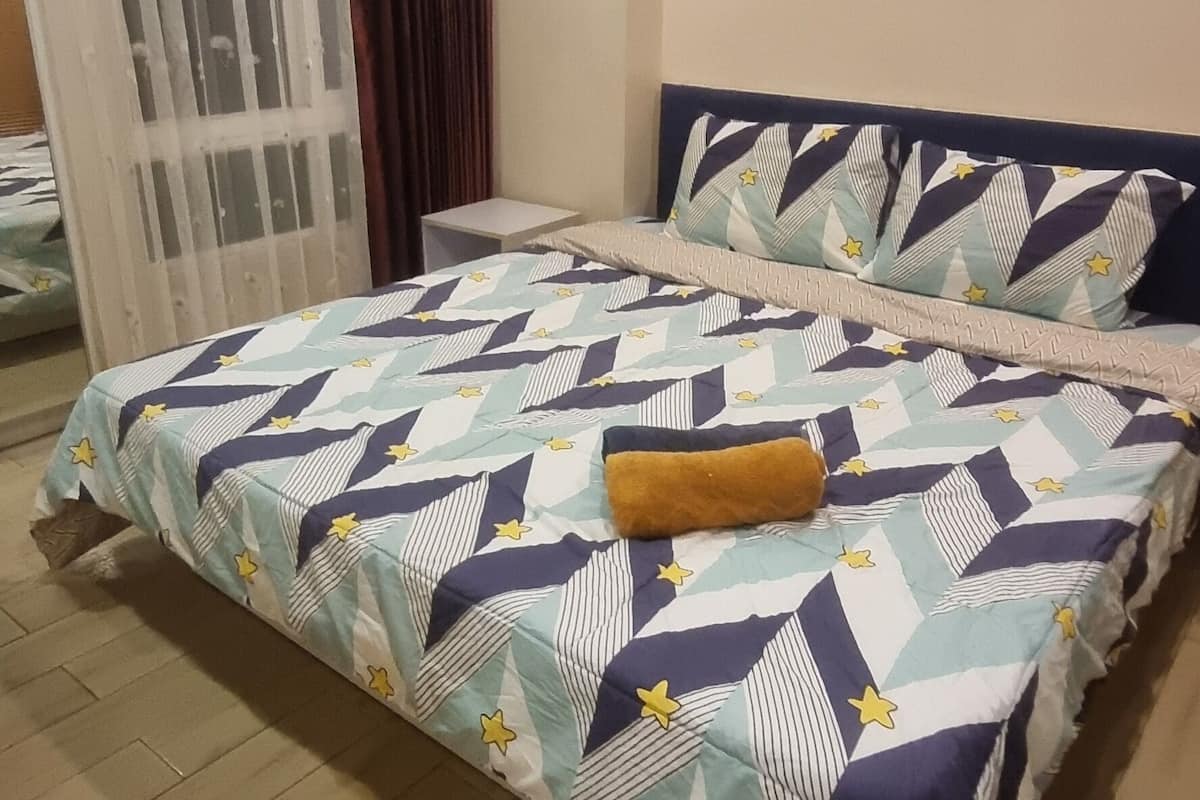 Une chambre à coucher avec un lit, une petite table de chevet, une fenêtre avec des rideaux et un luminaire au plafond.