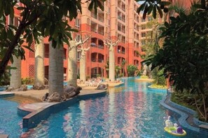 Una piscina de diseño curvo, rodeada de palmeras y un edificio de varios pisos con balcones.