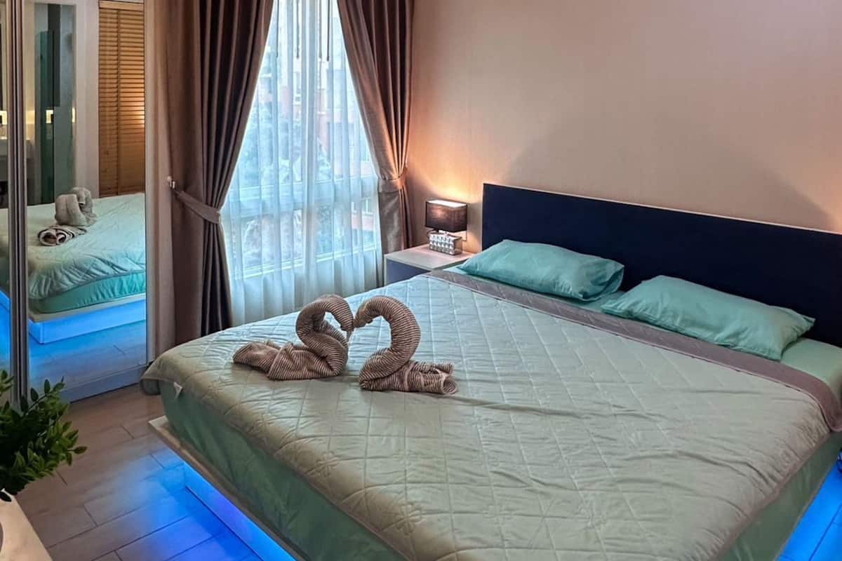 Une chambre d’hôtel moderne avec un grand lit, une table de chevet, une commode, un miroir et une vue sur l’extérieur.